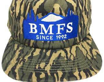 May include: A camouflage baseball cap with a blue and white embroidered patch that says "BMFS SINCE 1992".