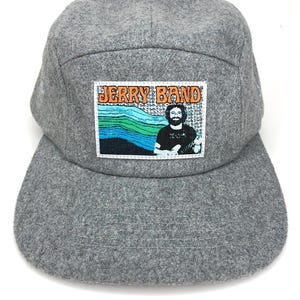 May include: A gray wool 5-panel cap with a patch featuring a photo of Jerry Garcia and the text "Jerry Band" in orange.