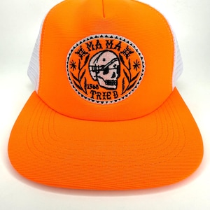 May include: Bright orange trucker hat with a white mesh back and a curved brim. The front features a circular patch with a skull wearing an eye patch, surrounded by the words "MAMA TRIED 1968".
