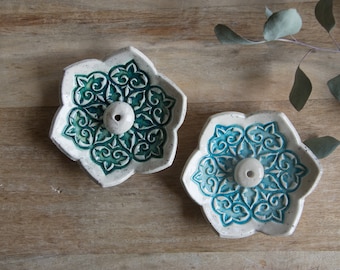 May include: Two white ceramic incense holders with a blue and green floral design. Each holder has a small hole in the centre for incense cones.