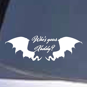May include: White vinyl decal featuring a stylized bat-like design with the text "Who's your Daddy?" in a cursive font. The decal is designed to be applied to a car window or similar surface.