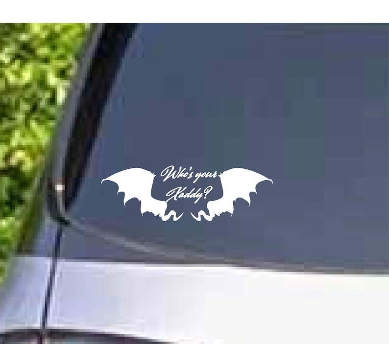 May include: White vinyl decal featuring a stylized bat-like design with the text "Who's your Daddy?" in a cursive font. The decal is designed to be applied to a car window or similar surface.