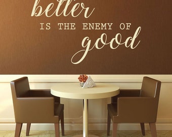 May include: A brown wall with the text "better is the enemy of good" written in white cursive lettering. Two brown leather chairs are positioned on either side of a round, white table with a silver base.