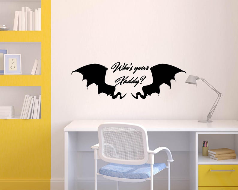 May include: A black wall decal featuring stylized bat wings with the text "Who's your Daddy?" in a cursive font. The decal is mounted on a white wall above a white desk with a chair and a desk lamp.
