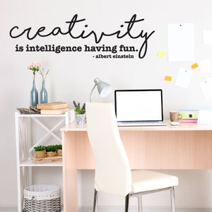 May include: A white desk with a laptop, a lamp, and a chair. There is a quote on the wall that says "Creativity is intelligence having fun. - Albert Einstein".