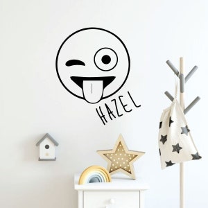 May include: Black and white wall decal of a winking emoji with its tongue sticking out. The name "Hazel" is written below the emoji.