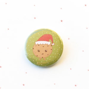 Peut inclure: Un bouton vert à pois blancs représente un biscuit de dessin animé portant un bonnet de Père Noël rouge. Le biscuit a des yeux bruns et un petit sourire.