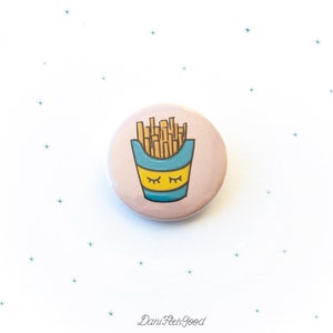 Op de afbeelding: Een roze knoop met een cartoonillustratie van een blauwe en gele container met frietjes met gesloten ogen. De container is gevuld met bruine frietjes.