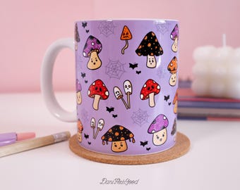 May include: A purple ceramic mug with a Halloween-themed design featuring cartoon mushrooms with different colored caps and faces. The mug has a white handle and is sitting on a cork coaster.