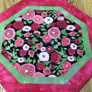 May include: Octagonal table runner with a green and pink border. The center features a black fabric with a floral pattern of red poppies, pink flowers, and green leaves.