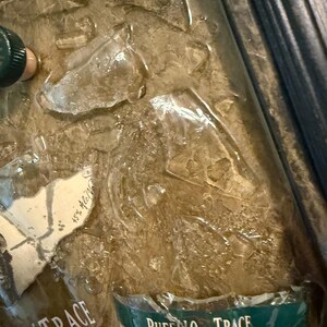 May include: A close-up of a bottle of Buffalo Trace Kentucky Bourbon Whiskey, with a green and white label. The bottle is partially submerged in ice. The label reads "Buffalo Trace" and "Kentucky Straight Bourbon Whiskey".