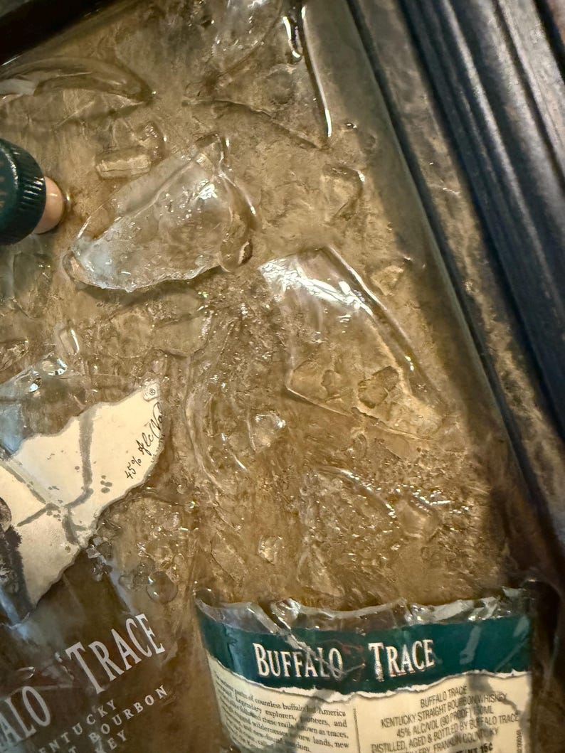 May include: A close-up of a bottle of Buffalo Trace Kentucky Bourbon Whiskey, with a green and white label. The bottle is partially submerged in ice. The label reads "Buffalo Trace" and "Kentucky Straight Bourbon Whiskey".