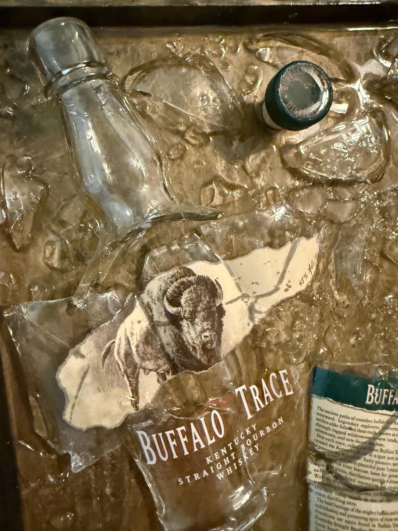 May include: A clear glass bottle and a green-topped cap are set against a textured, golden-brown background. The label for "Buffalo Trace Kentucky Straight Bourbon Whiskey" is visible, featuring a bison illustration.