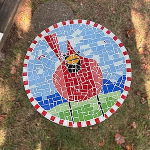 May include: A mosaic table top featuring a red cardinal bird design. The bird is surrounded by blue, green and white mosaic tiles. The table top has a white and red striped border.