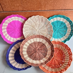 Puede incluir: Seis platos de mimbre tejido con acentos coloridos. Los platos son redondos y tienen una textura tejida natural. Los colores son rosa, blanco, azul verdoso, marrón, azul y naranja.