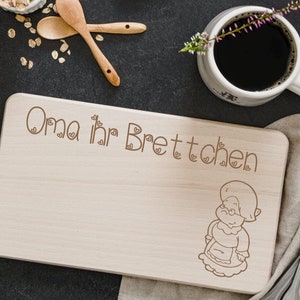 Puede incluir: Una tabla de cortar de madera con el texto "Oma ihr Brettchen" y una ilustración de dibujos animados de una mujer con un vestido y un delantal.