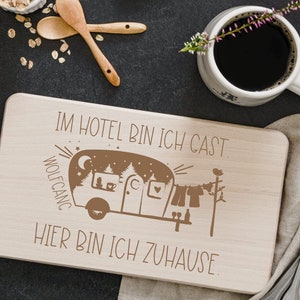 Pode incluir: Uma tábua de cortar de madeira com um design gravado em marrom de uma caravana com o texto "Im Hotel bin ich Gast, hier bin ich zu Hause".