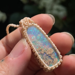 May include: A white opal pendant with a light blue and green iridescent sheen, set in a white macrame cord.