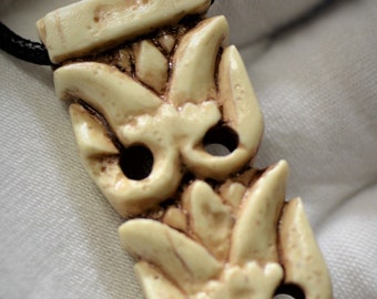 May include: A cream-colored pendant necklace with a detailed carved design of three stylized flowers. The pendant is attached to a black cord.