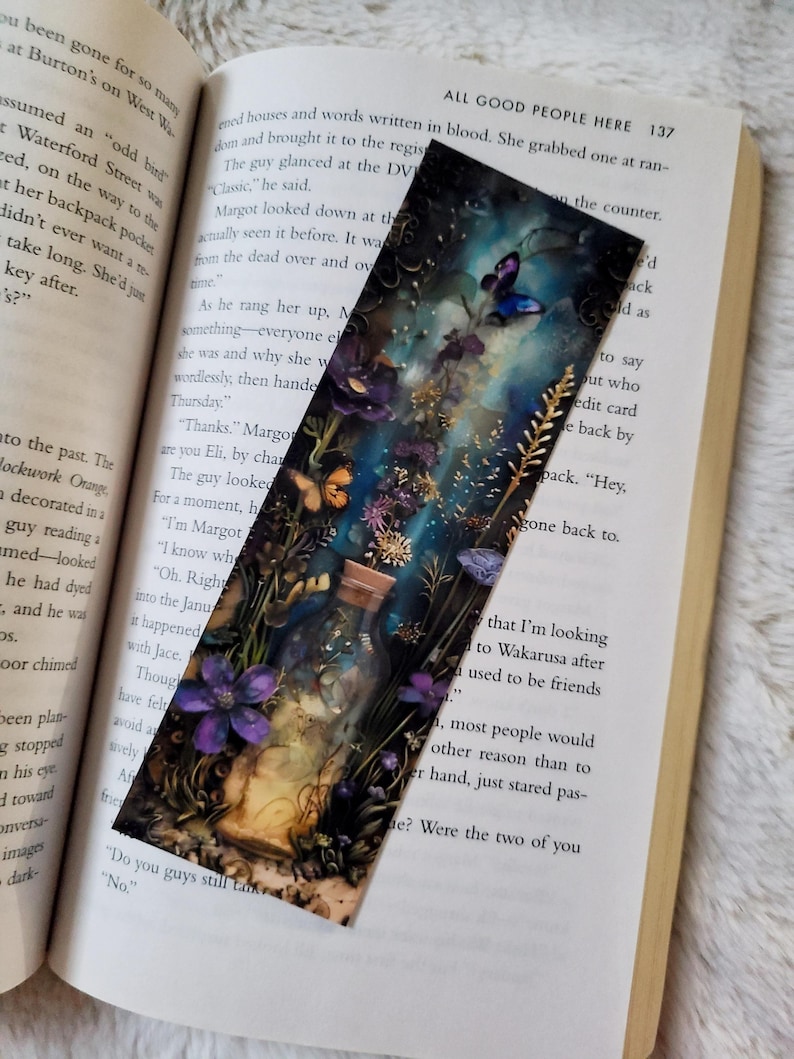 K&ouml;nnte beinhalten: Dekorativer Lesezeichen mit einer fantastischen Illustration eines Glases voller Blumen und Schmetterlinge. Das Kunstwerk hat eine dunkle, vertr&auml;umte &Auml;sthetik mit Farbt&ouml;nen von Lila, Blau und Gold. Das Lesezeichen befindet sich in einem offenen Buch.