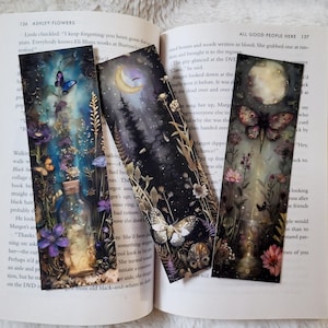 K&ouml;nnte beinhalten: Drei dekorative Lesezeichen mit Illustrationen zum Thema Natur. Eines zeigt einen mondbeschienenen Wald, ein anderes einen Schmetterling mit Blumen und das dritte eine Flasche mit Blumen und Schmetterlingen. Die Lesezeichen liegen auf einem offenen Buch mit Text.