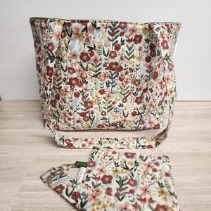 May include: A floral print tote bag and matching coin purse. The bag has a long shoulder strap and a green interior lining. The floral pattern features red, yellow, and pink flowers on a cream background. The coin purse has a silver key ring.