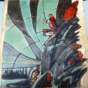 Könnte beinhalten: Ein Keramikfliesenmosaik mit einer Libelle und einem Schmetterling. Das Kunstwerk verwendet eine Palette aus Schwarz, Grün und Rot. Die Libelle und der Schmetterling haben rote und weiße Flügel. Der Hintergrund ist ein geometrisches Muster.