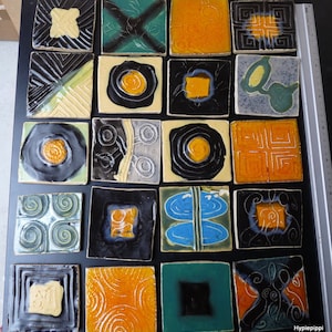 May include: A collection of twenty-one square ceramic tiles with various abstract designs. The tiles feature a range of colors, including black, yellow, orange, green, and blue. Each tile has a unique pattern, such as swirls, geometric shapes, and floral motifs.