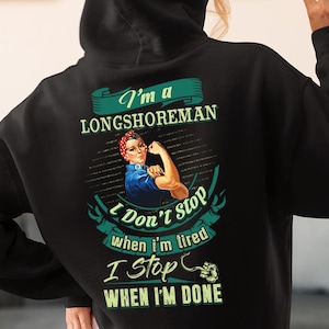 Puede incluir: Sudadera con capucha negra con el texto "I'm a Longshoreman" y un gráfico de una mujer flexionando el brazo. La parte trasera también muestra el texto "I Don't Stop when I'm tired, I Stop when I'm Done".