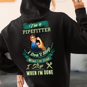 Puede incluir: Sudadera con capucha negra con un gráfico en la espalda que dice "I'm a Pipefitter" encima de una imagen al estilo de Rosie the Riveter. Debajo de la imagen, el texto dice "I Don't Stop When I'm Tired, I Stop When I'm Done."