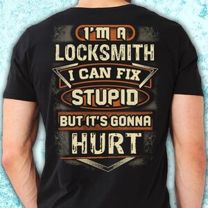 Puede incluir: Camiseta negra con un diseño desgastado. La camiseta presenta el texto "I'M A LOCKSMITH I CAN FIX STUPID BUT IT'S GONNA HURT" en letras blancas y naranjas. El diseño tiene un aspecto vintage y desgastado.