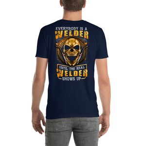 May include: A navy blue t-shirt with a gold skull graphic and the text "Everybody is a Welder Until the Real Welder Shows Up".
