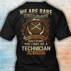 May include: A black short-sleeved t-shirt featuring a graphic design with a wrench and screwdriver. The text reads: WE ARE RARE, We are Smart, WE ARE LEGENDS, SUCK IT UP MOFO, YOU CAN'T BE A TECHNICIAN AND A PUSSY in tan and white lettering.