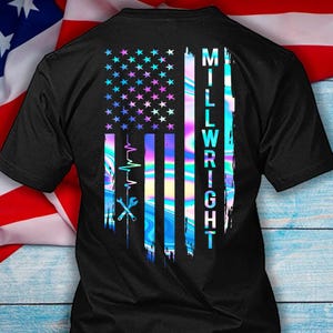 May include: Black t-shirt with a design resembling the American flag, rendered in iridescent colours. The design includes stars, stripes, the word "MILLWRIGHT", a wrench, and a heartbeat graphic. The overall effect is a modern, patriotic theme.