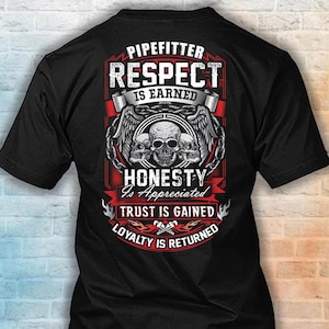 May include: A black short-sleeved t-shirt featuring a graphic on the back with three skulls, wings, and chains. The text reads: PIPEFITTER RESPECT IS EARNED HONESTY Is Appreciated TRUST IS GAINED LOYALTY IS RETURNED, with crossed pipe wrenches.
