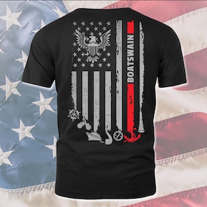 May include: Black t-shirt with a distressed American flag design. The flag has a red stripe with the word "BOATSWAIN" written vertically. The flag also features a bald eagle, a ship's wheel, binoculars, a ship, a compass, and an anchor.