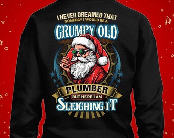 Pode incluir: Camisola preta com um gráfico do Pai Natal com óculos de sol e um cachimbo. O texto diz: "I NEVER DREAMED THAT SOMEDAY I WOULD BE A GRUMPY OLD PLUMBER BUT HERE I AM SLEIGHING IT."