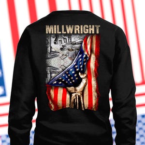 Puede incluir: Camiseta negra de manga larga con un diseño gráfico. El diseño incluye el texto "MILLWRIGHT", una bandera estadounidense, una mano y herramientas. La bandera es roja, blanca y azul.