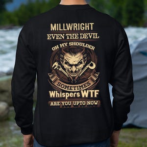 Op de afbeelding: Zwart sweatshirt met een grafisch ontwerp op de achterkant. Het ontwerp bevat de tekst "MILLWRIGHT EVEN THE DEVIL ON MY SHOULDER SOMETIMES Whispers WTF ARE YOU UPTO NOW" met een duivelsgezicht en gereedschap.