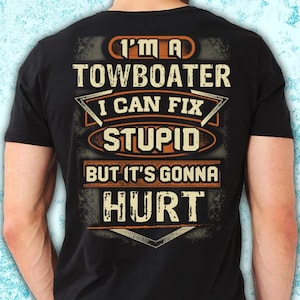 May include: Black t-shirt with the text "I'M A TOWBOATER I CAN FIX STUPID BUT IT'S GONNA HURT" in orange and white lettering. The design has a distressed, vintage look.