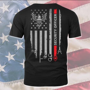 Könnte beinhalten: Ein schwarzes T-Shirt mit einer Grafik einer abgenutzten amerikanischen Flagge. Die Streifen bestehen aus einer Handfeuerwaffe, einem Schlagstock, Handschellen, einem roten Streifen mit dem Text SECURITY OFFICER und Schlüsseln. Ein Adler ist abgebildet.