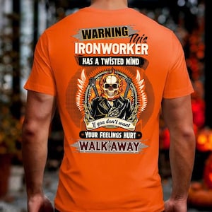 May include: Orange t-shirt with a graphic on the back. The graphic features a skull with flames, tools, and the text "WARNING IRONWORKER HAS A TWISTED MIND" and "If you don't want YOUR FEELINGS HURT WALK AWAY."
