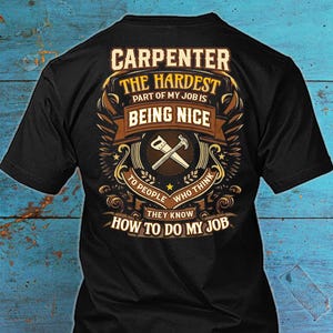 May include: Black t-shirt with a carpenter-themed design. The design features text that reads "CARPENTER THE HARDEST PART OF MY JOB IS BEING NICE" with a hammer and saw graphic.