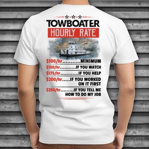 May include: White t-shirt featuring the text "TOWBOATER HOURLY RATE" in black and red. Below the text is an image of a towboat on the water. The shirt also lists hourly rates based on involvement in the job.