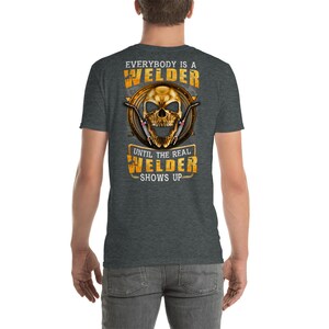 May include: A dark heather grey t-shirt with a skull graphic and the text "Everybody is a Welder Until the Real Welder Shows Up".