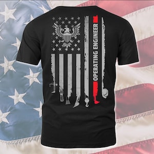 May include: Black t-shirt with a distressed American flag design. The flag has a bald eagle in the center and the words "OPERATING ENGINEER" on the right side. The flag is surrounded by various tools, including a level, a wrench, and a crane hook.