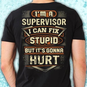May include: Black t-shirt featuring the text "I'M A SUPERVISOR I CAN FIX STUPID BUT IT'S GONNA HURT" in orange and white. The design has a distressed, vintage aesthetic.