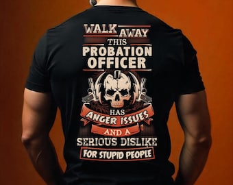 Puede incluir: Camiseta negra con el texto "WALK AWAY THIS PROBATION OFFICER HAS ANGER ISSUES AND A SERIOUS DISLIKE FOR STUPID PEOPLE." El diseño incluye una calavera, pistolas y pancartas decorativas.