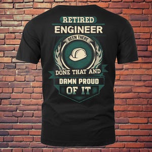 Op de afbeelding: Zwart t-shirt met een ontwerp voor een gepensioneerde ingenieur. Het ontwerp bevat de tekst "Retired Engineer Been There Done That And Damn Proud Of It" en een symbool van een veiligheidshelm.