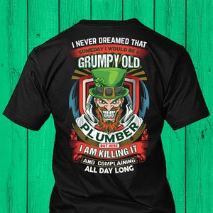 May include: Black t-shirt with a graphic featuring a grumpy leprechaun wearing a green hat and the text "I NEVER DREAMED THAT SOMEDAY I WOULD BE A GRUMPY OLD PLUMBER BUT HERE I AM KILLING IT AND COMPLAINING ALL DAY LONG."